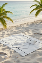 White towel and hand  towel on a sandy beach with palm trees and ocean in the background